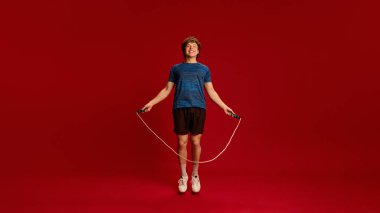 Havada ip atlayan enerjik bir adam, Kırmızı Stüdyo 'nun arka planına karşı dinamik kardiyo sırasında gülümsüyor. Atlama egzersizi, dayanıklılık, sağlıklı yaşam tarzı, çeviklik eğitimi kavramı.