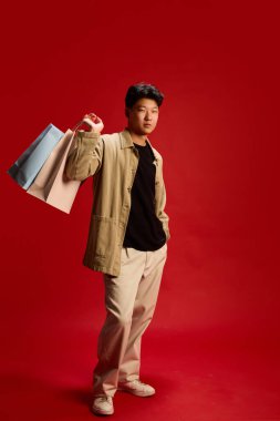 Alış veriş torbalarıyla poz veren şık genç bir adam, kendinden emin bir şekilde kameraya bakıyor. Moda kavramı, satış sezonu, perakende terapisi, nüfuz, marka, alışveriş kültürü, yaşam tarzı.