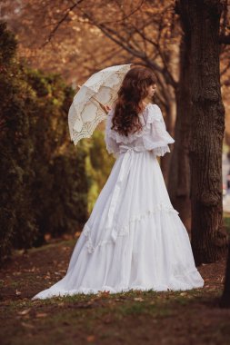 Sonbahar ağaçları arasında dantel şemsiyeli, klasik beyaz elbiseli zarif bir kadın hareket halinde donmuştu. Fantezi kavramı, tarih, kayıp aşk, akıldan çıkmayan hafıza. Kitaplar ve film kapakları için uygun.