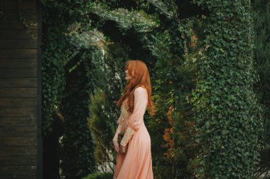 Romantik şeftali rengi elbiseli bir kadının yeşil kemerin altında gözleri kapalı duruşu. Gizli özlem kavramı, yumuşak güzellik, duygusal durgunluk. Fantezi roman ya da film için uygun.