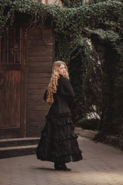 Viktorya dönemi siyah korseli zarif kadın, gölgeler ve eski ahşap ile çevrili sarmaşık kemer altında sabit bir bakışla döner. Zarafet kavramı, gotik romantizm. Tarihsel, fantezi kapağı için mükemmel.