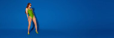 Pankart. Yeşil mayo giymiş ince kızıl saçlı manken, geriye doğru eğiliyor, mavi arka planda negatif alan ile duruyor. Yaz kavramı, tatil, tatil, moda ve tarz.