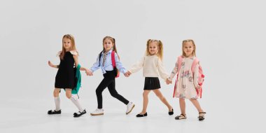 Bir grup neşeli kız koordine okul kıyafetleri ve sırt çantalarıyla beyaz stüdyo geçmişine karşı birlikte poz veriyorlar. Öğrenim kavramı, eğitim, okula dönüş, kütüphane, yeni fikirler.