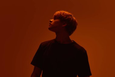 Keskin gölgeleri olan genç bir adamın silueti ve yükselen arka planda sıcak neon ışıkta dik dik bakan bir bakış. Güzellik, ifade, duygusal yalnızlık, kimlik, derinlik, öz farkındalık kavramı.