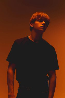 Yakışıklı genç adamın portresi öne eğilmiş, başı eğik, karamsar, sıcak ışıklandırma kasları eğimli arka planda poz veriyor. Güzellik kavramı, duygular, nostalji.