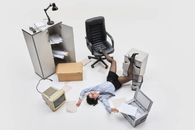 Ofis çalışanı kağıt yığınının arasında yere yığıldı. Bir bacağı kaotik iş ortamında kabinede kaldırıldı. İş dünyasında aşırı çalışma, yorgunluk ve absürt baskı kavramı.