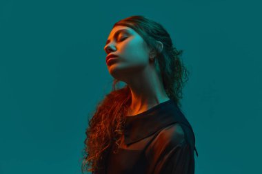 Şehvetli, güzel bir kadının portresi. Kapalı gözlerle poz veriyor. Turuncu ışıkta turuncu zemine yaslanmış rahat duruyor. Güzellik anlayışı, insani duygular, moda. Ad