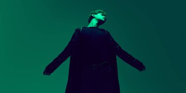 Yeşil stüdyoda kollarını esneten erkek modelin geniş açılı portresi ve parlak neon ışıklı silüet. Güzellik ve moda kavramı, kendini ifade etme, insani duygular.