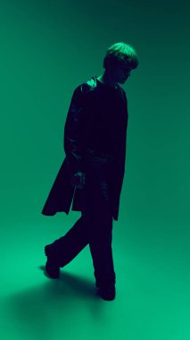 Yeşil ışıkta öne çıkan genç adam portresi dramatik bir kontrastla ve deniz mavisi arkaplanına karşı paltoyla. Güzellik ve moda kavramı, kendini ifade etme, insani duygular.