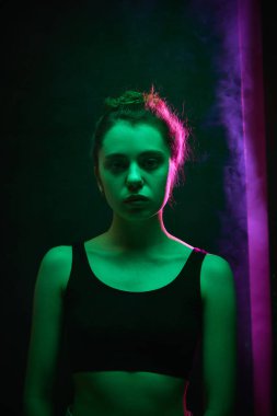 Saçları birbirine bağlı genç bir kadın, canlı pembe arka ışığın altında kasvetli sinematik ışıklandırmada karanlık stüdyo duvarına bakıyor. Güzellik ve moda kavramı, kendini ifade etme, insani duygular.