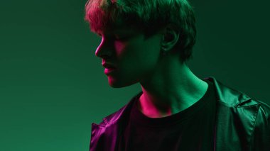 Canlı morumsu morlar altında huzurlu yüzü olan genç bir adamın yan profili ve yumuşak gölgeli, eğimli arka plana karşı şık deri ceketli yeşil ışıklar. Duyguların kavramı, kendini ifade etme.