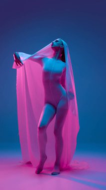 Genç dansçı kollarını uzatır ve parlak neon ışıkta katıksız kumaş ile insan zarafetini gradyan arka planda harmanlar. Özgürlük kavramı, bale, hareketin güzelliği, dansın duygusal ruhu.
