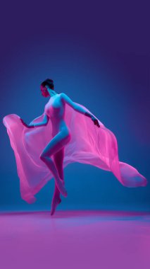 Dar beyaz tulum giymiş genç bir kadın, hareket özgürlüğünü sembolize eden, gradyan mavi stüdyo arka planına karşı pembe kumaşla dans ediyor. Güzellik, dans, müzik kavramı.