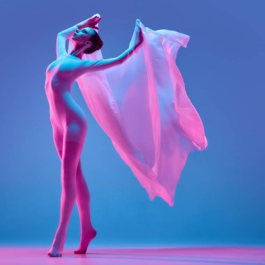 Genç kadın, fütüristik neon atmosferde kadınsı enerji ve gücü sembolize eden mavi arkaplana doğru ilerlerken uçan pembe kumaşı tutuyor. Bale dansı konsepti müzik güzellik özgürlüğü