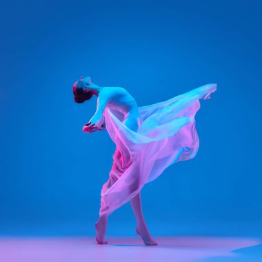 Kadın narin kumaşı yumuşak neon lambaların altında tutarak zarif bir performans sergiliyor ve enerji ve zarafet hissi yaratıyor. Güzellik, bale, müzik, dans, estetik, özgürlük, hareket kavramı.