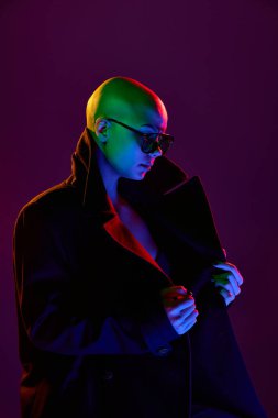 Aşırı büyük ceketli, neon gölgeli kel ve çekici bir kadın elinde yakasıyla gizemli bir çekicilik sergiliyor. Duyguların kavramı, kendini ifade etme, kadınlık, tarz, moda, gelecekçilik.