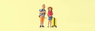 Pankart. Sırt çantalı ve çantalı şık bir kız ve erkek, sarı arka planda, negatif alanlı, kendinden emin görünüyorlar. Çocukluk kavramı, seyahat, tatil, macera, sağlık, eğlence.