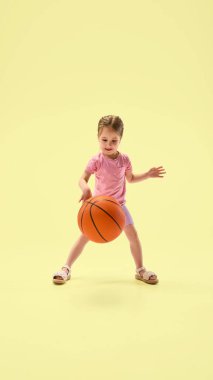 Stüdyoda sarı arka planda gülümserken basketbola odaklanmış bir kız. Dinamik fotoğraf. Genç şampiyon. Çocukluk kavramı, spor, eğlence, yaz, sağlık, hareket.