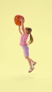 Odaklanmış bir kızın açık duruşu ve Pastel Stüdyo arka planında etkileyici duruşu ile basketbolu sektirme fotoğrafının tüm vücudu. Çocukluk kavramı, yaz, spor, özgürlük, sağlık, hareket, oyun.