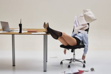 Beyaz stüdyo arka planına karşı ofis saatinde bacaklarıyla gazetelere gömülmüş genç bir kadın. Ofis hayatı kavramı, insan duyguları, sosyal meseleler, iş.