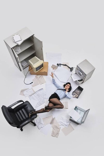 Фото с воздуха. Женщина-офисный работник лежит на полу с свободным галстуком и бумагами, разбросанными по хаотичному месту работы. Концепция офисного образа жизни, человеческих эмоций, социальных проблем, бизнеса.