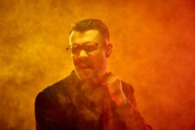 Çizgili takım elbiseli bir adam, renkli dumanların arasında sanki basınç altında kopuyormuş gibi duygusal olarak kravatını çeker. Yaratıcı bir portre. Yorgunluk, gerginlik, zihinsel yorgunluk, psikolojik stres kavramı.