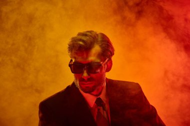 Saçları dağınık ve güneş gözlüklü bir adam yoğun sis ve neon ışıklarıyla çevrili tedirgin bir ifadeyle aşağıya bakıyor. Gizli duygular kavramı, içsel karanlık, endişe, erkek psikolojisi, imajı.