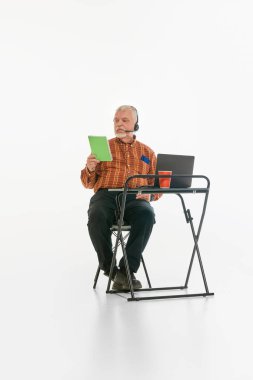 Son sınıf öğretmeni kulaklık takıyor, online derste notlar okuyor ve beyaz stüdyo geçmişine karşı çıkıyor. Uzaktan öğrenme. Akademik, olgun eğitim, çevrimiçi sunum kavramı.