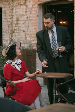 Zarif ve yakışıklı bir erkek, güzel bir kadına bakarken cam verir. İkisi de şık, eski moda kıyafetler giyer. Birbirine aşık klasik bir çift. İlk randevu. Bağbozumu, aşk, nostalji kavramı.