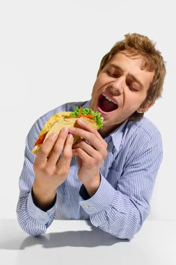 Taze sebzelerle ve beyaz arka planda kocaman ağzı olan lezzetli dolgulu taco dürümünü ısırmak üzere olan bir adam. Fast food, paket yemek, beslenme, geleneksel.
