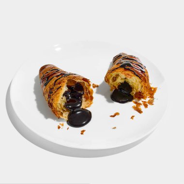 Çikolata dolu kruvasan, beyaz arka planda altın kırıntılarla çevrili, yüzeye sızan parlak siyah dolgulu bir tabakta dilimlenmiş. Geleneksel, fast food kavramı..