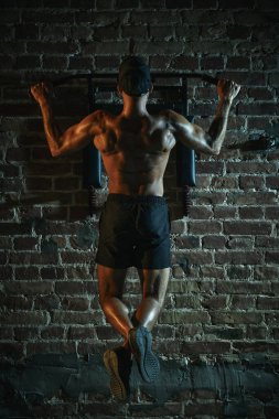 Arkadan bakan adam barfiks çekiyor, kaslı sırtında barfiks çekiyor, dramatik ışık altında parlıyor, kendini işine adamış ve güçlü bir fiziği var. Spor anlayışı, aktif ve sağlıklı yaşam tarzı