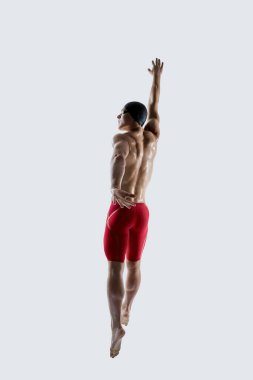 Güçlü erkek yüzücü, kollarını tamamen uzatmış ve odaklanmış bir şekilde beyaz stüdyo arka planına doğru yükselir. Spor eğitimi kavramı, esneklik, güven, güç