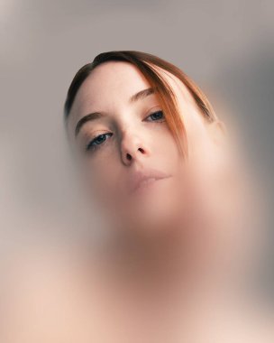 Kavramsal sanat eserleri. Kızıl saçlı, delen mavi gözlü bir kadının portresi bulanık filtreden aşağıya bakıyor, izolasyon ve içgözlem iletiyor. Güzellik ve psikoloji kavramı.