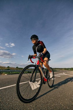 Düşük açılı fotoğrafta kadın bisikletçi virajlı yolda, eller alt gidona, agresif yarış duruşu ve gözlerde odaklanma görülüyor. Bisiklet, güç, motivasyon, yol, spor kavramı.