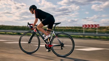Düz yolda bisikletçinin dinamik fotoğrafı yumuşak gökyüzünde sürüşü ve arka planda aksanlı hareket hızıyla bariyerler. Hareket bulanıklığı etkisi. Yarış, hareket, adrenalin, bisiklet, rekabet kavramı.