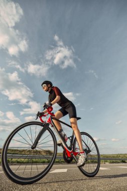 Düşük açılı fotoğraf, güneşli otoyolda hareket eden kadın bisikletçi, aerodinamik poziyon vurgu hareketi. Spor, hız, güven, denge, performans, yaşam tarzı kavramı.