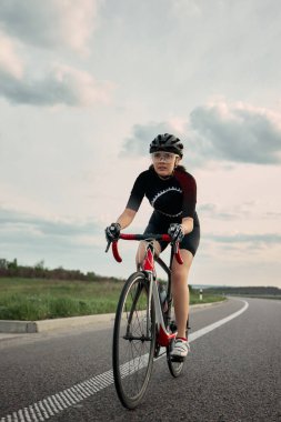 Bisikletçi güçlü bir kavramayla öne doğru eğiliyor, hareketler aktif anda donuyor, fırtınalı bulutlar ve bariyer eğrisi önümüzde. Spor, hareket, güç, odaklanma, hız kavramı. Ad