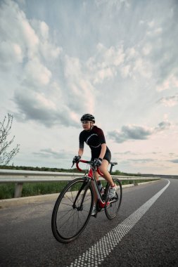 Kendinden emin bir kız, tam teçhizatlı bir bisikletçi açık kırsal yolda ilerliyor, güçlü adımlar atıyor ve hedefe odaklanmış gözler ileride. Bağlılık, spor, hareket, fitness yolculuğu kavramı.
