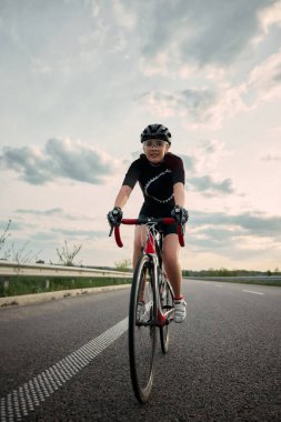 Gülümseyen kadın bisikletçi, atletizm kıyafetleri ve güvenlik kaskı takmış, gece ışığında güvenli bir şekilde yol bisikletine biniyor. Spor, hareket, yaşam tarzı, enerji kavramı.