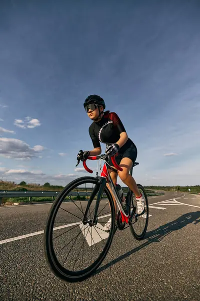 Düşük açılı fotoğrafta kadın bisikletçi virajlı yolda, eller alt gidona, agresif yarış duruşu ve gözlerde odaklanma görülüyor. Bisiklet, güç, motivasyon, yol, spor kavramı.