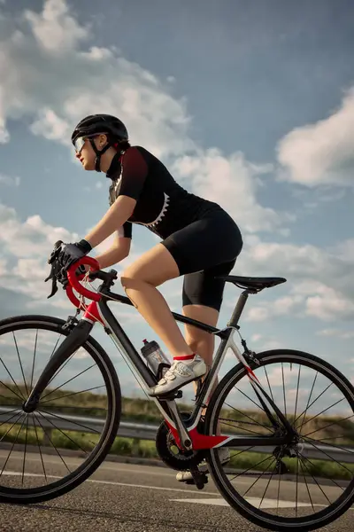 Bisikletçinin parlak gökyüzünün altında bisiklet sürerken, temiz otoyolda ilerlerken, pedal hareketine odaklanarak altın ışıkta yakalanırken yan görüntüsü. Özgürlük kavramı, dayanıklılık, açık hava.