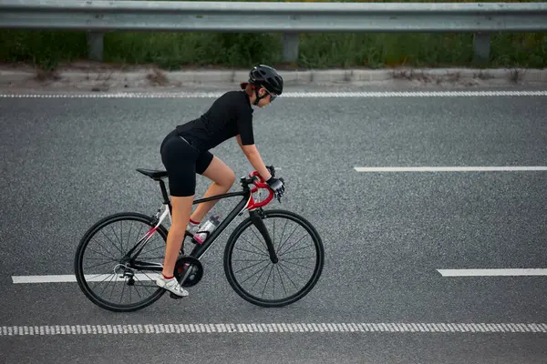 Yan görüntü fotoğrafı. Otoyoldaki bariyerlerin önünden geçen kadın bisikletçi antrenmanlara odaklanmış. Hareket bulanıklığı etkisi. Spor eğitimi kavramı, disiplin, bisiklet çabası, odaklanma