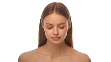 Doğal güzellik. Yumuşak, sağlıklı tenli, beyaz stüdyo arka planına karşı yumuşak bir gülümsemeyle bakan sakin genç bir kadının yakın çekimi. Moda anlayışı, saç bakımı, cilt bakımı, iç denge