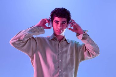 Gündelik giysiler giyen genç çocuk, hafif bir gülümsemeyle kulaklık takıyor, değişken arkaplana karşı neon ışığı altında müzik dinlemenin tadını çıkarıyor. Mutluluk kavramı, rahatlama, neşe