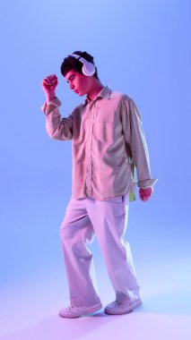 Büyük tişörtlü çocuk müzik ve dans dinliyor, eğik kollu ritmik bir şekilde hareket ediyor, neon ışığa daldırılmış, eğimli arka planda. Oyunculuk, rahatlama, rahatlama kavramı.