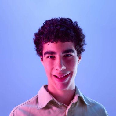 Yumuşak bukleli, parlak gözlü, gülümseyen bir çocuğun yakın plan fotoğrafı, kameraya ince bir tebessümle bakıyor. İnsani duygular, mutluluk, sakinlik kavramı