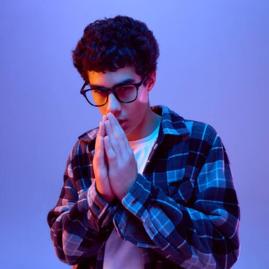 Gözlüklü genç, umut dolu bir jestle el ele tutuşuyor. Eğilim geçmişine karşı odaklanmış ve ciddi bir ruh hali içinde. Konsantrasyon, umut, huzur, düşünceli duygu kavramı.