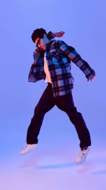 Neşeli ve mutlu atlayan genç bir çocuğun dinamik fotoğrafı, neon ışıkta eğimli arka plana karşı şaşkınlık ve neon dolu. Hareket kavramı, olumlu duygular, başarı, gençlik havası