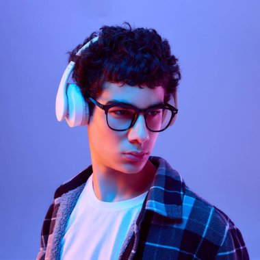 Gözlüklü ve kulaklıklı çocuğun ciddi bir ifadeyle yakın çekimi, derinlemesine odaklanmayı ya da değişken arkaplana karşı neon ışığındaki kararlılığı gösteriyor. İnsan duyguları kavramı odaklanma, dijital